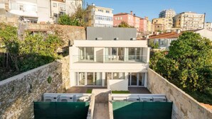 A modern two-story building with a glass facade, surrounded by greenery and adjacent to a stone wall. - 5 Fervença Boutique Palace Flats by HostWise (Vila Nova de Gaia)