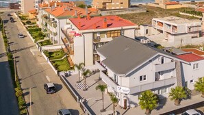 Ett bostadsområde vid kusten med moderna byggnader, en gata med parkerade bilar och utsikt över havet.