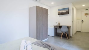A hotel room with a bed, a desk, a chair, a TV, and a wardrobe.