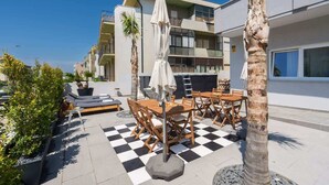 A rooftop terrace with outdoor seating, palm trees, and a checkered floor.