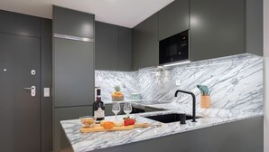 A modern kitchen with dark cabinetry, a marble countertop, and a built-in microwave.