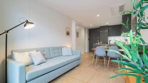 A modern living room with a light blue sofa, a floor lamp, and a dining area with a table and chairs.
