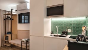 Une chambre d’hôtel compacte comprenant un coin cuisine, un espace salon avec un canapé et une petite table, ainsi qu’une fenêtre avec des rideaux.