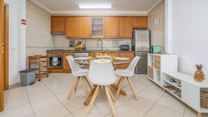 A compact kitchen with wooden cabinets, a dining table with chairs, a refrigerator, and a microwave. - Bright & Comfortable Flat by HostWise (Santa Luzia)
