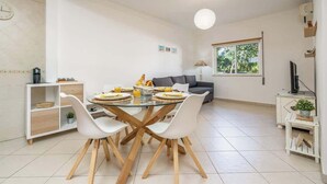 A dining area with a glass table, white chairs, and a grey sofa in the background. - Bright & Comfortable Flat by HostWise (Santa Luzia)
