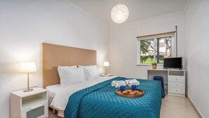A hotel room with a bed, bedside tables, a desk with a TV, and a window with a view of greenery. - Bright & Comfortable Flat by HostWise (Santa Luzia)