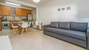 A modern kitchen with wooden cabinets, a dining area with white chairs, a grey sofa, and a white pendant light. - Bright & Comfortable Flat by HostWise (Santa Luzia)