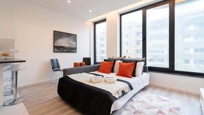 A modern hotel room with a large bed, a desk, and a chair. There are two large windows providing a view of the city. - Trendy Spacious Flat by HostWise (Matosinhos)