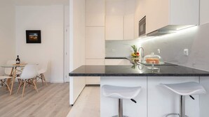 A modern kitchen with white cabinetry, a black countertop, and a dining area with a table and chairs. - Trendy Spacious Flat by HostWise (Matosinhos)