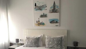 A hotel room with a bed, two bedside tables, a nightstand, a wall-mounted artwork depicting a cityscape, and a window with curtains. - Host Wise Arvore - Room w/ Terrace & Pool (Árvore)