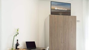 A modern room with a wooden desk, a laptop, a chair, a bottle of wine, and a television displaying 'hostwise'. - Host Wise Arvore - Triple Room w/ Terrace & Pool (Árvore)