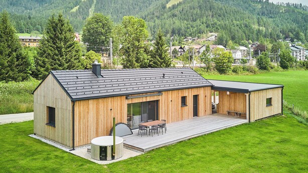A modern wooden building with a flat roof, a covered outdoor seating area, and a view of a green hillside in the background. - Chalet Hochsteiermark (Mariazell)