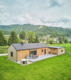 A modern wooden building with a flat roof, a covered outdoor seating area, and a view of a green hillside in the background. - Chalet Hochsteiermark (Mariazell)