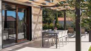 A covered outdoor dining area with a stone wall, a glass door, and a table with chairs. - Villa Casa Veritas with pool for 8 guests, quiet location, near Porec (Višnjan)