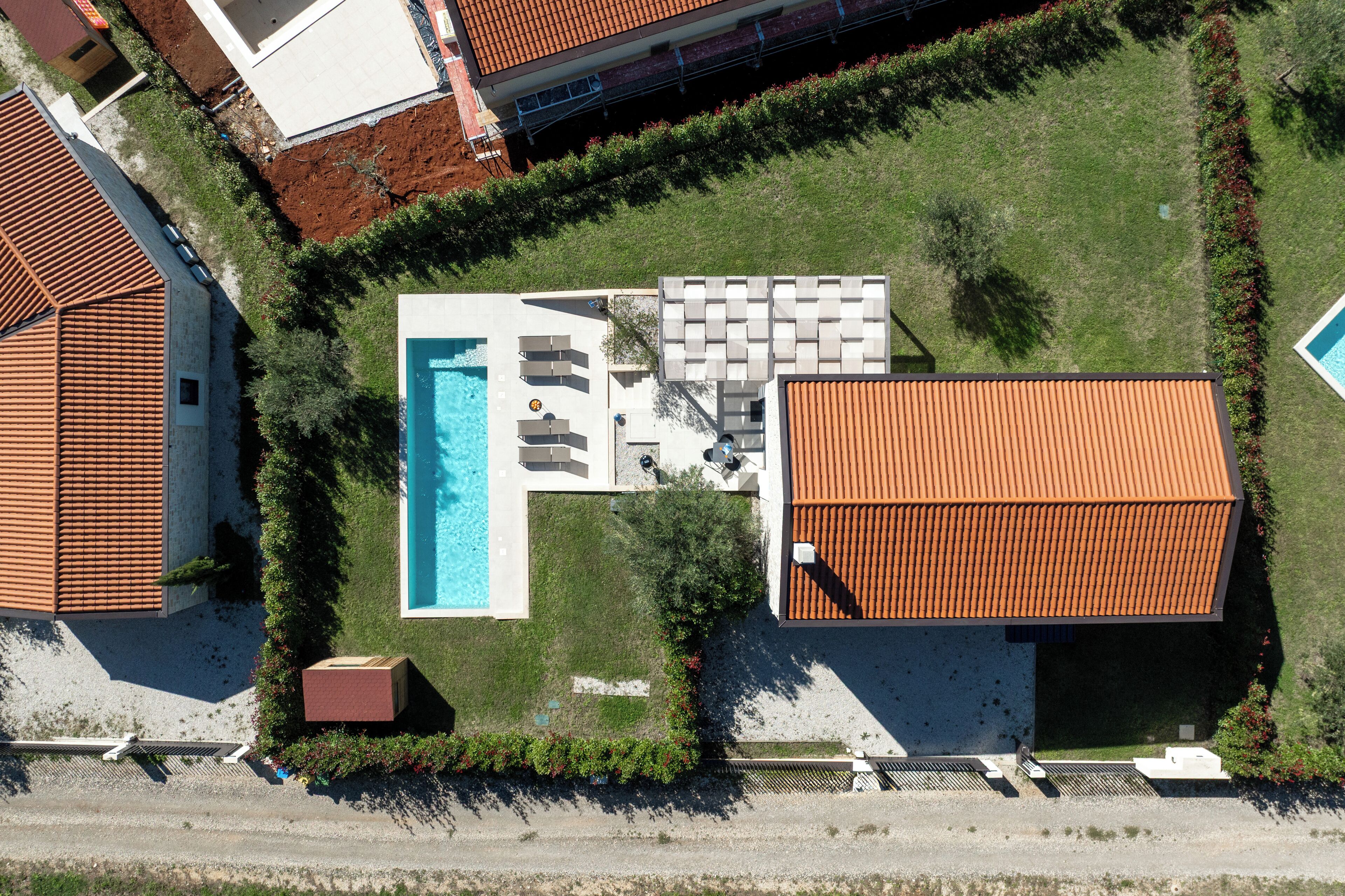 An aerial view of a property with a swimming pool, sun loungers, and a covered patio area.
