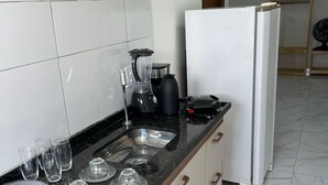 A kitchen with a black countertop, white cabinets, a sink, a coffee maker, and a white refrigerator. - Pousada e Flat Diamant's (Ipojuca)