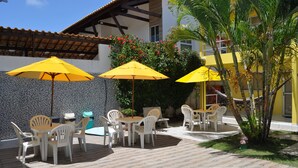 An outdoor patio area with a pool, yellow umbrellas, white plastic chairs, and a tiled floor. - Pousada e Flat Diamant's (Ipojuca)