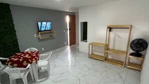 A spacious room with a tiled floor, a television mounted on the wall, and a wooden shelf unit. - Pousada e Flat Diamant's (Ipojuca)