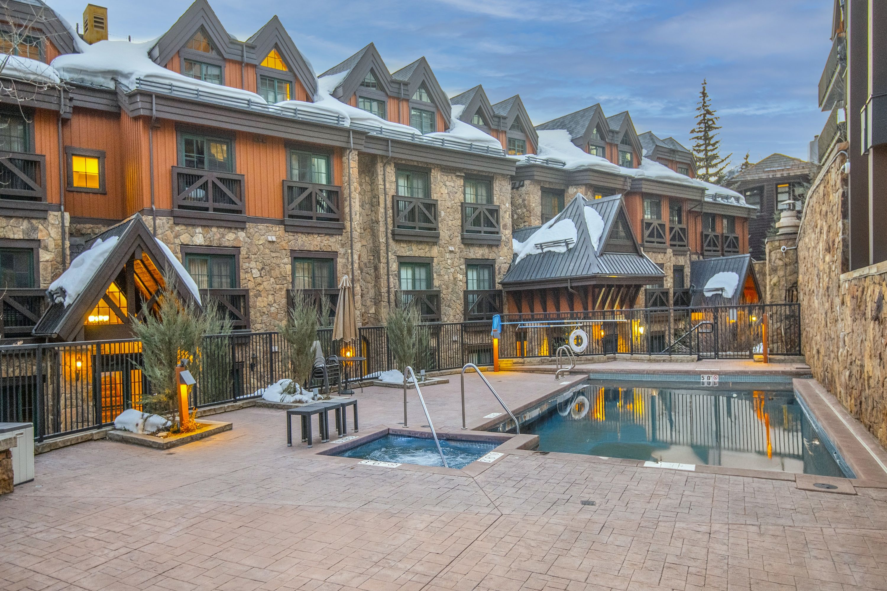 Un resort con piscina, edificios de piedra y madera, y zonas de estar al aire libre.