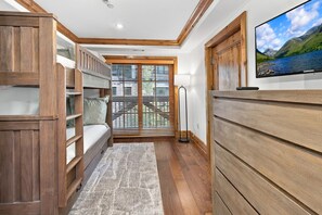 A room with a bunk bed, a television on the wall, and a window with blinds. - Vail Mountain View #402 4 Bedroom Condo (Vail)