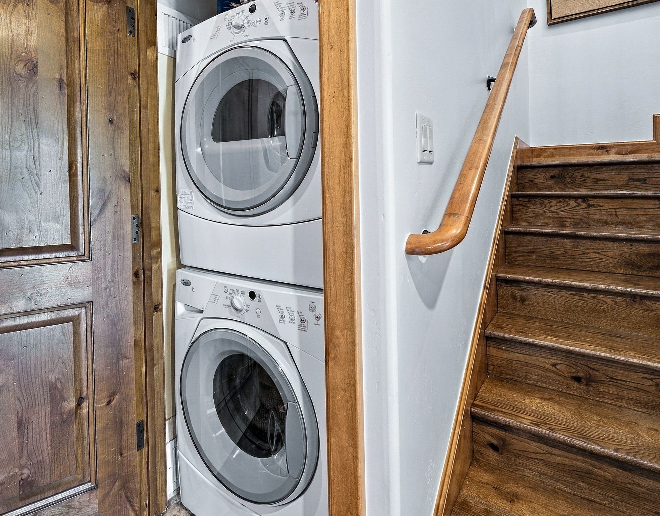 A laundry room with two front-loading washing machines, a wooden door, and a wooden staircase.