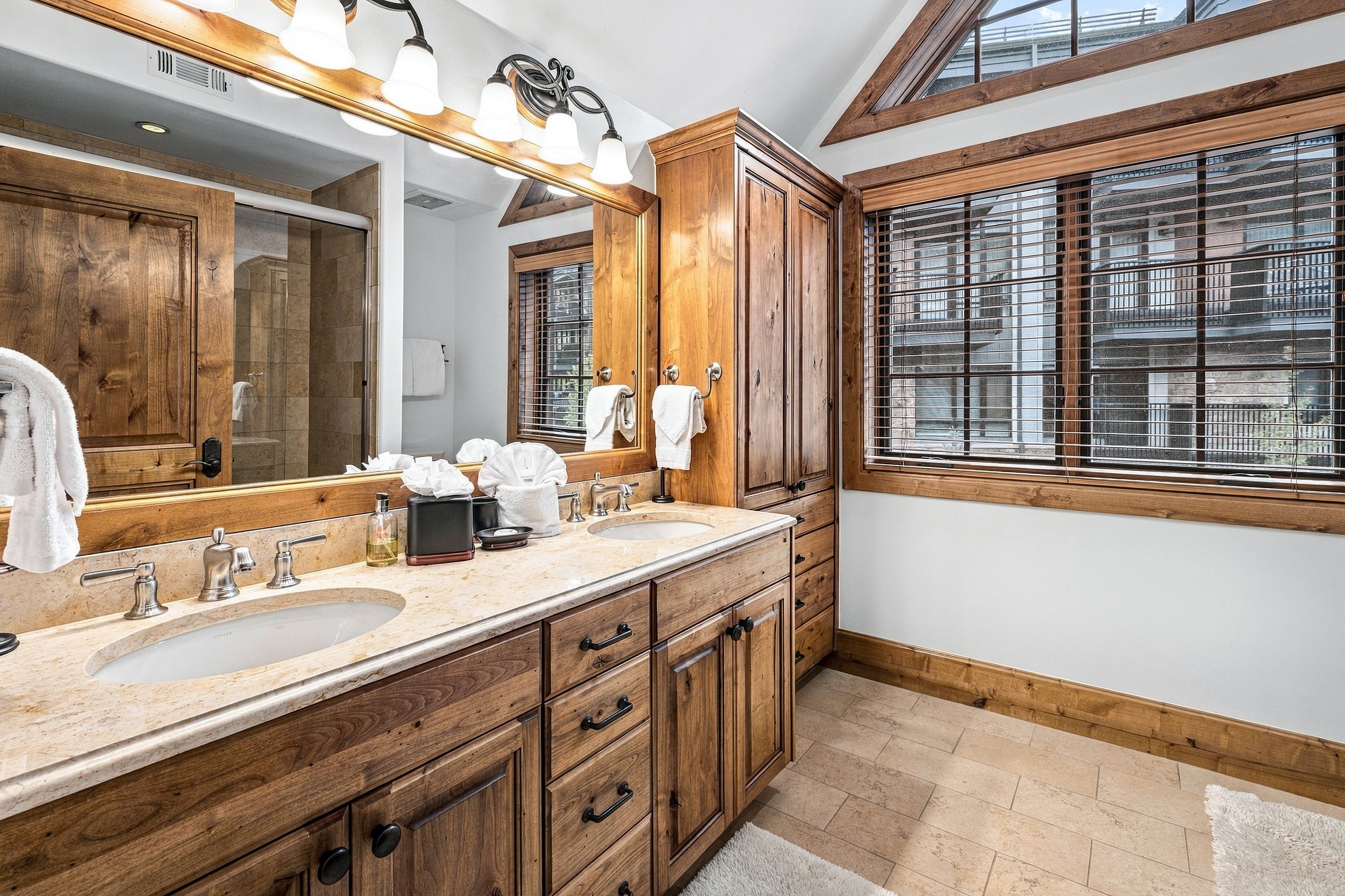 Un baño con muebles de madera, lavamanos doble y un espejo grande con iluminación.