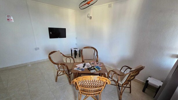 A dining area with a round table, four wicker chairs, a television on the wall, and a ceiling fan.