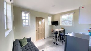Un espacio habitable compacto con sofá, una pequeña cocina y un televisor montado en la pared.