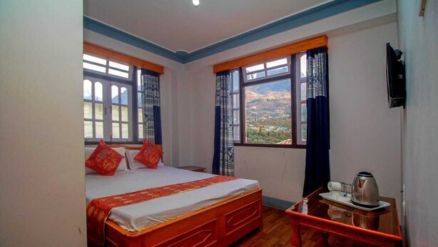 A hotel room with a bed, a small table with a kettle, and curtains on the windows. - Bon Kiputhang (Chungthang)