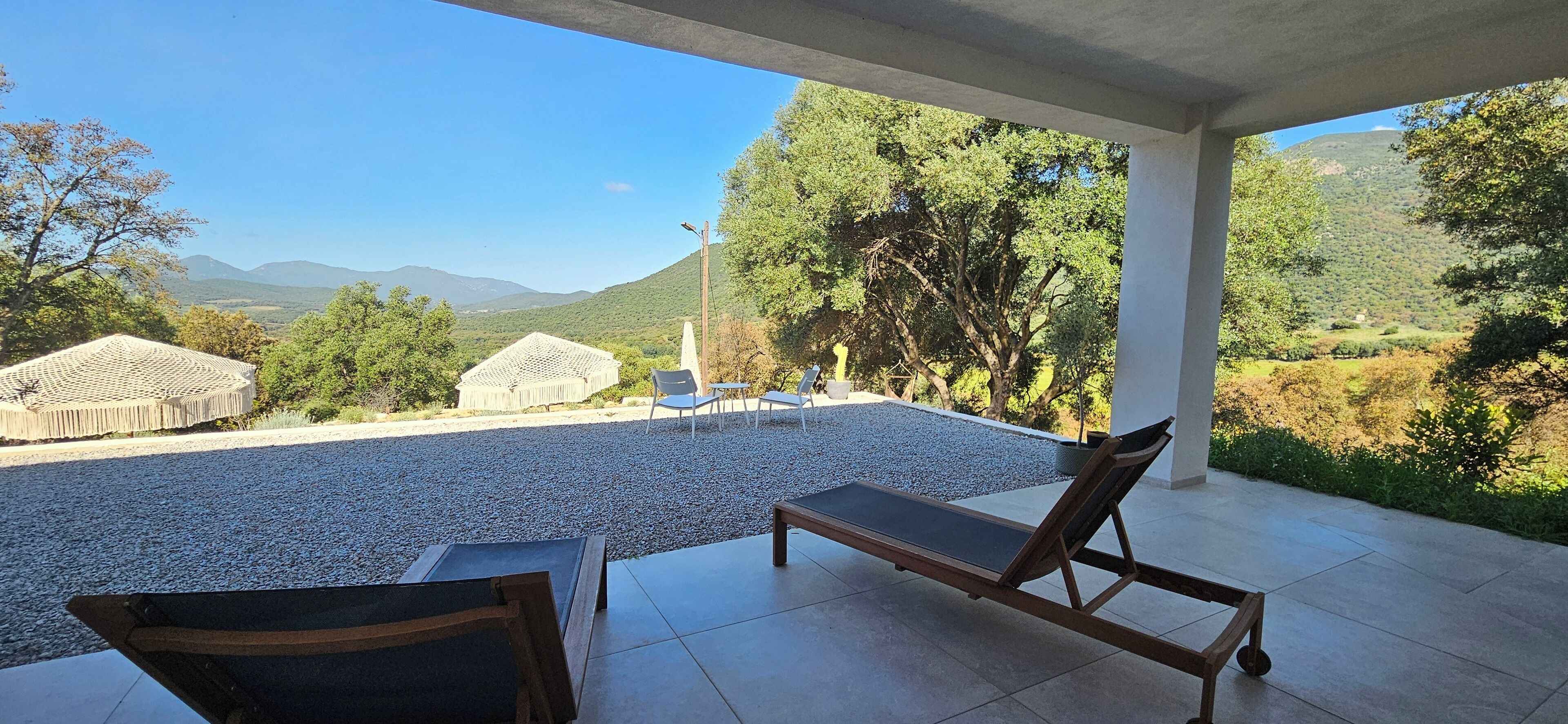 Un espacio al aire libre cubierto con un patio de grava, dos sillones de madera y una pequeña mesa.