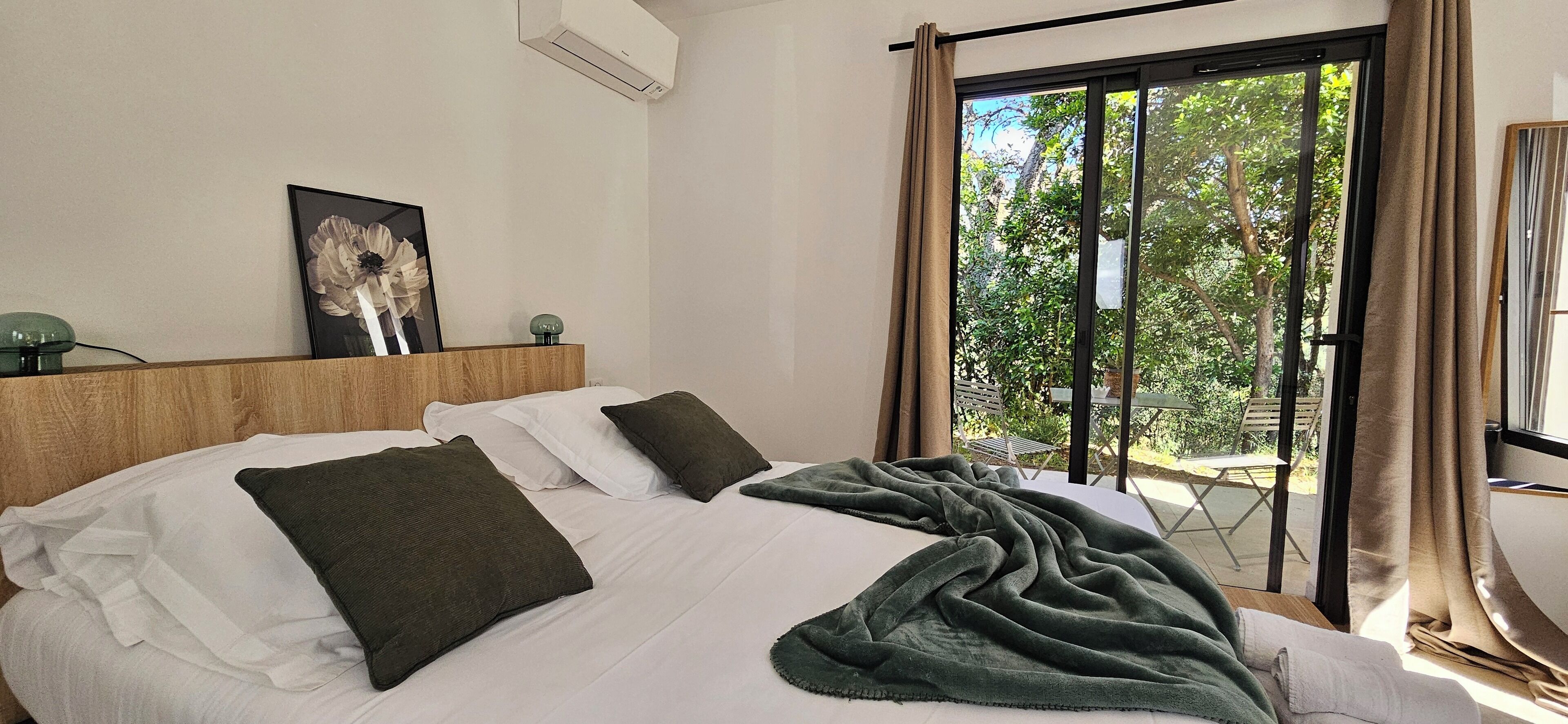 A hotel room with a large bed, a headboard, a framed picture, and a view of the outdoors through a sliding door.