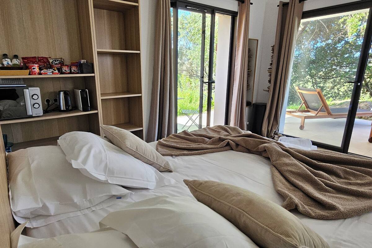 Een slaapkamer met een bed, nachtkastje, plank met toiletartikelen en uitzicht op het omliggende landschap.