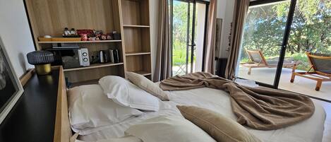 Quarto com cama, mesa de cabeceira, prateleira com artigos de higiene pessoal e vista para o exterior.