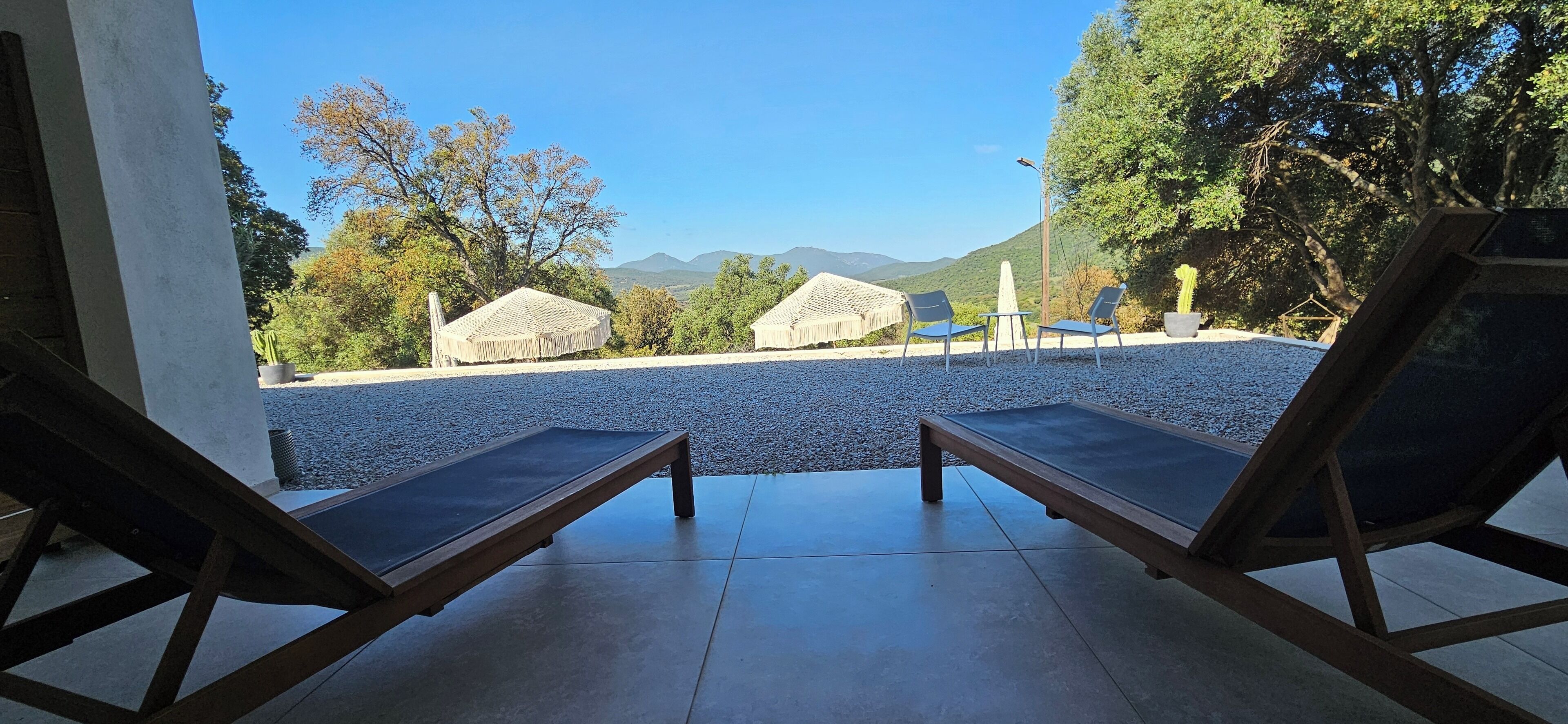 A poolside area with lounge chairs and thatched umbrellas, overlooking a mountainous landscape.