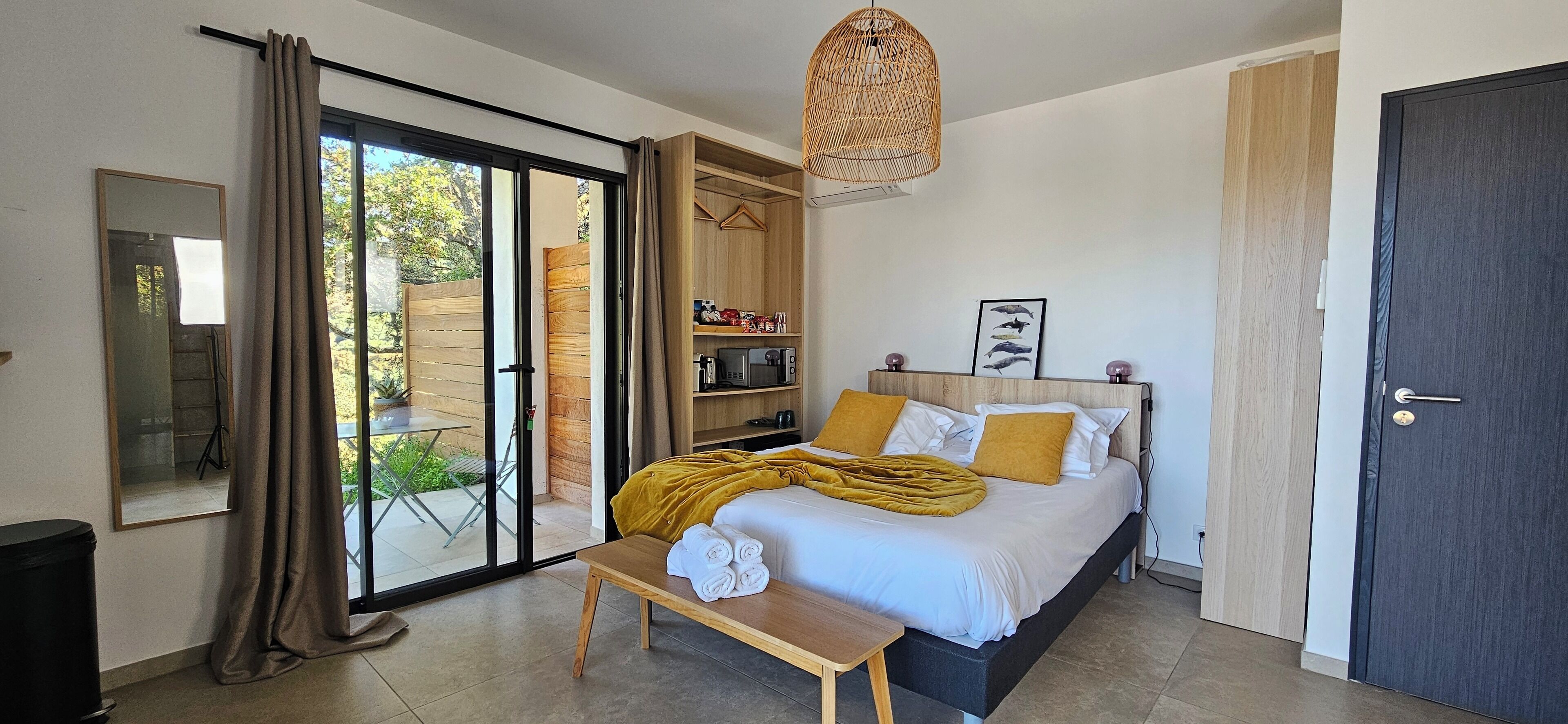 Une chambre à coucher comprenant un lit, une table, une armoire et une porte-fenêtre coulissante donnant sur un espace extérieur.