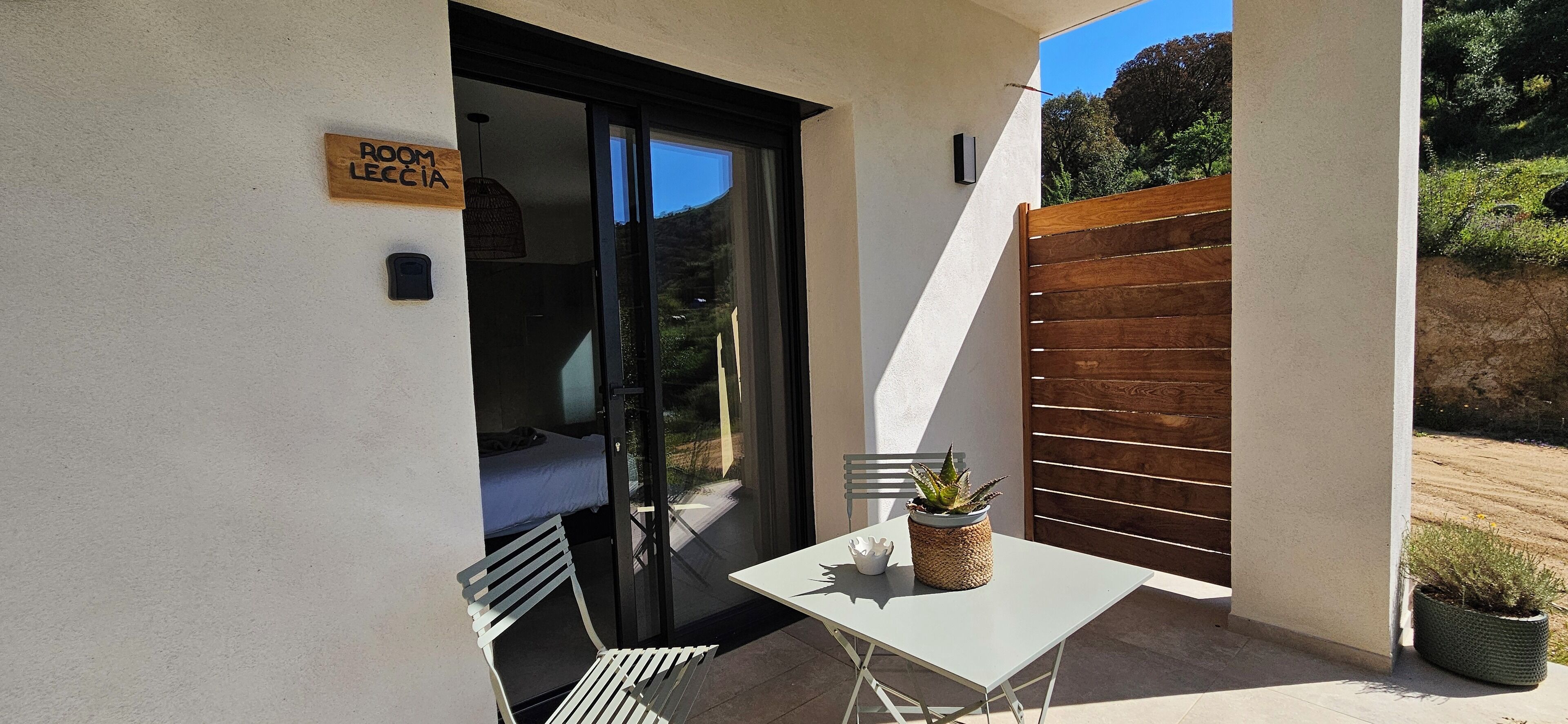 A small patio with a table, chairs, a potted plant, and a sliding glass door leading to a bedroom.