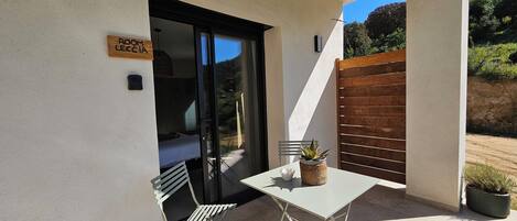 A small patio with a table, chairs, a potted plant, and a sliding glass door leading to a bedroom.