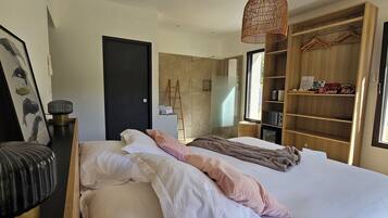 A modern bedroom with a large bed, a wardrobe, a bedside table, and a hanging light fixture.