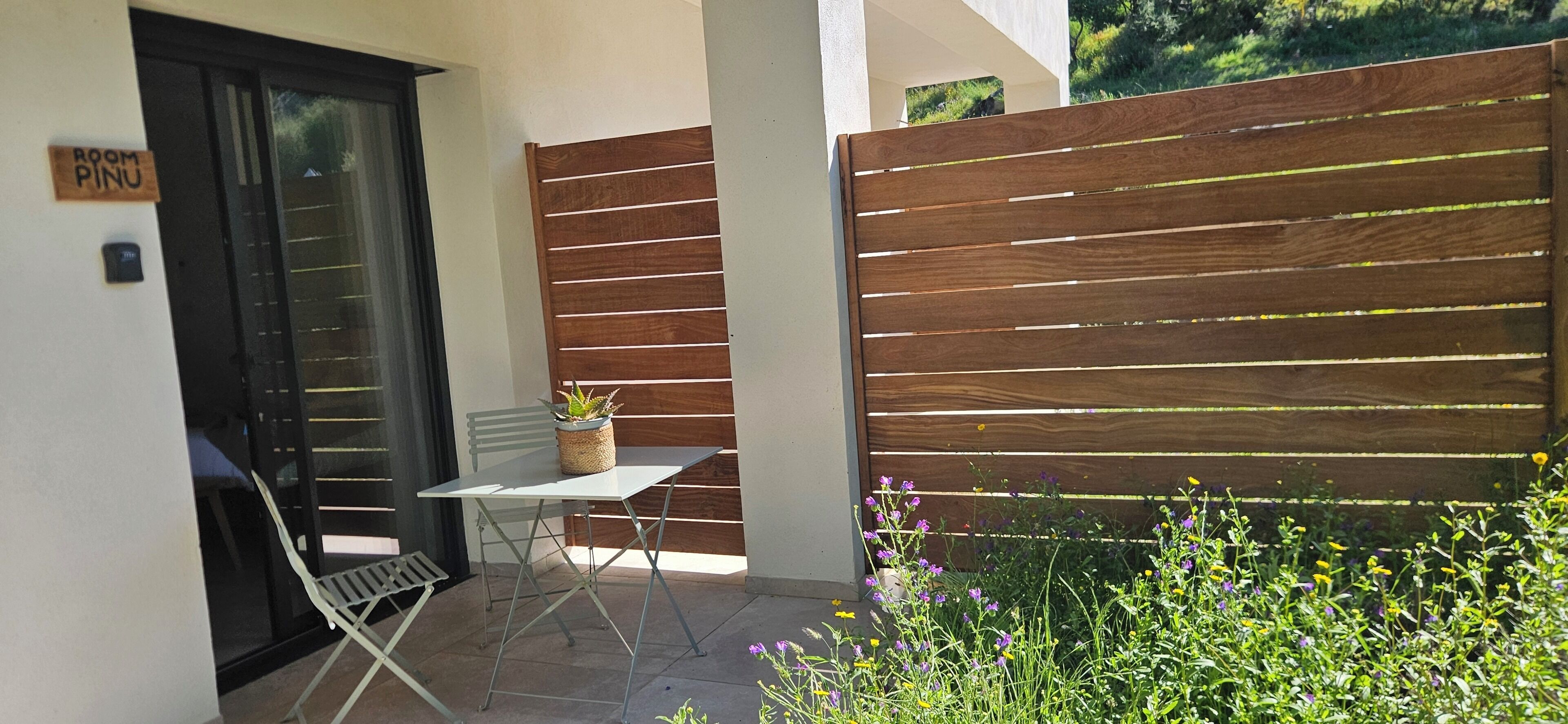 Eine Terrasse mit Tisch und Stühlen, ein Holzzaun und ein Schild mit der Aufschrift 'ROOM PINU'.