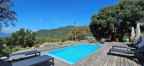 Une terrasse en bois avec une piscine rectangulaire, des chaises longues et une vue sur un paysage montagneux.
