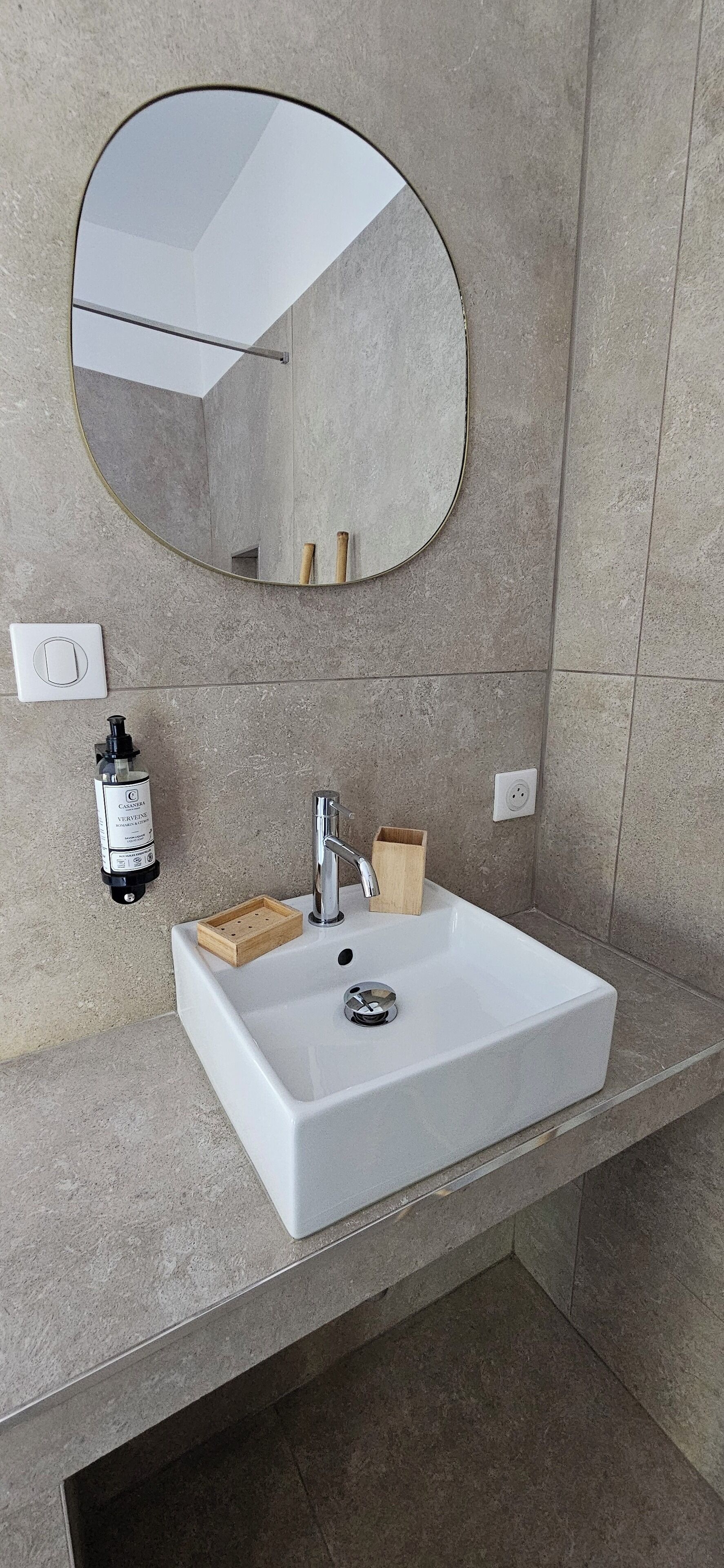 A bathroom with a white sink, a round mirror, and a wooden soap dish.