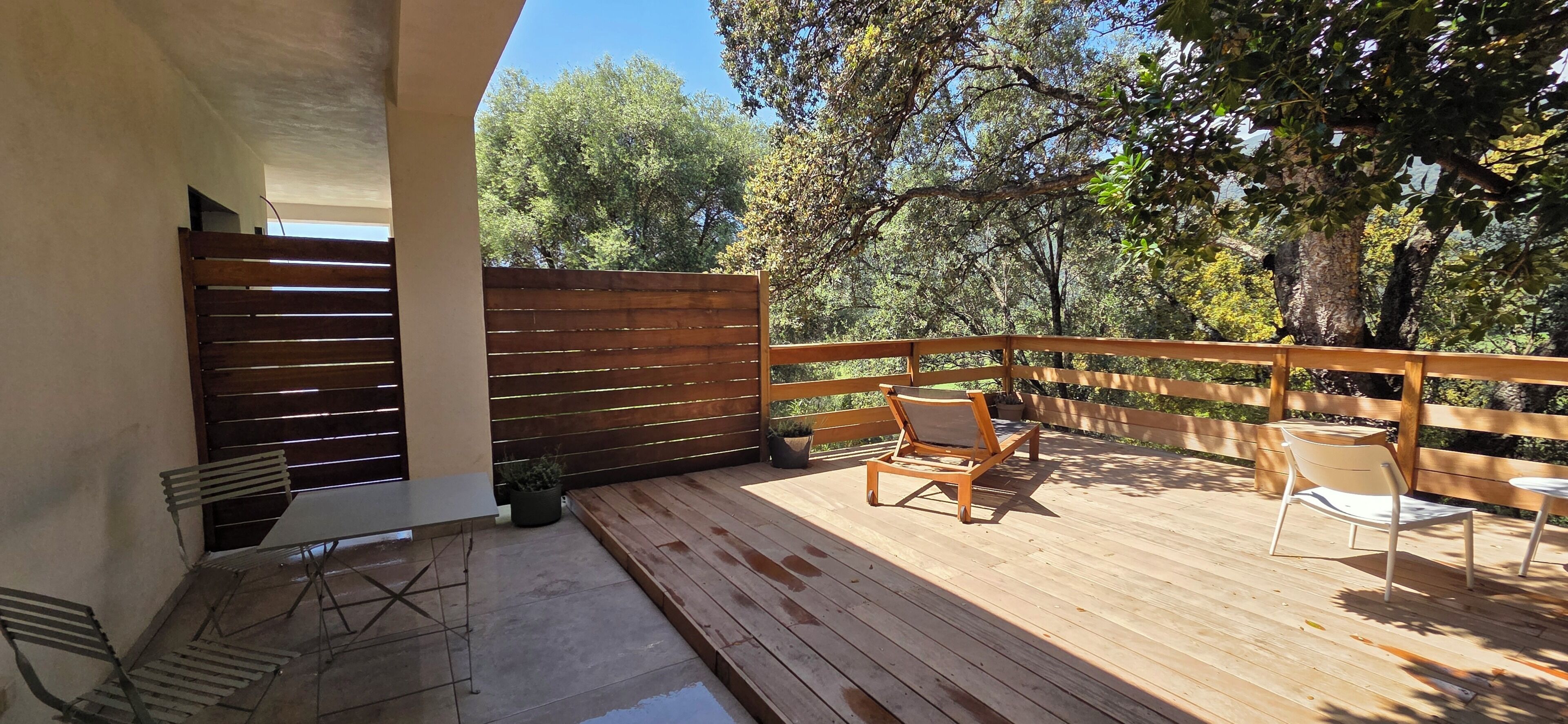 A wooden deck with a railing, two chairs, and a table.