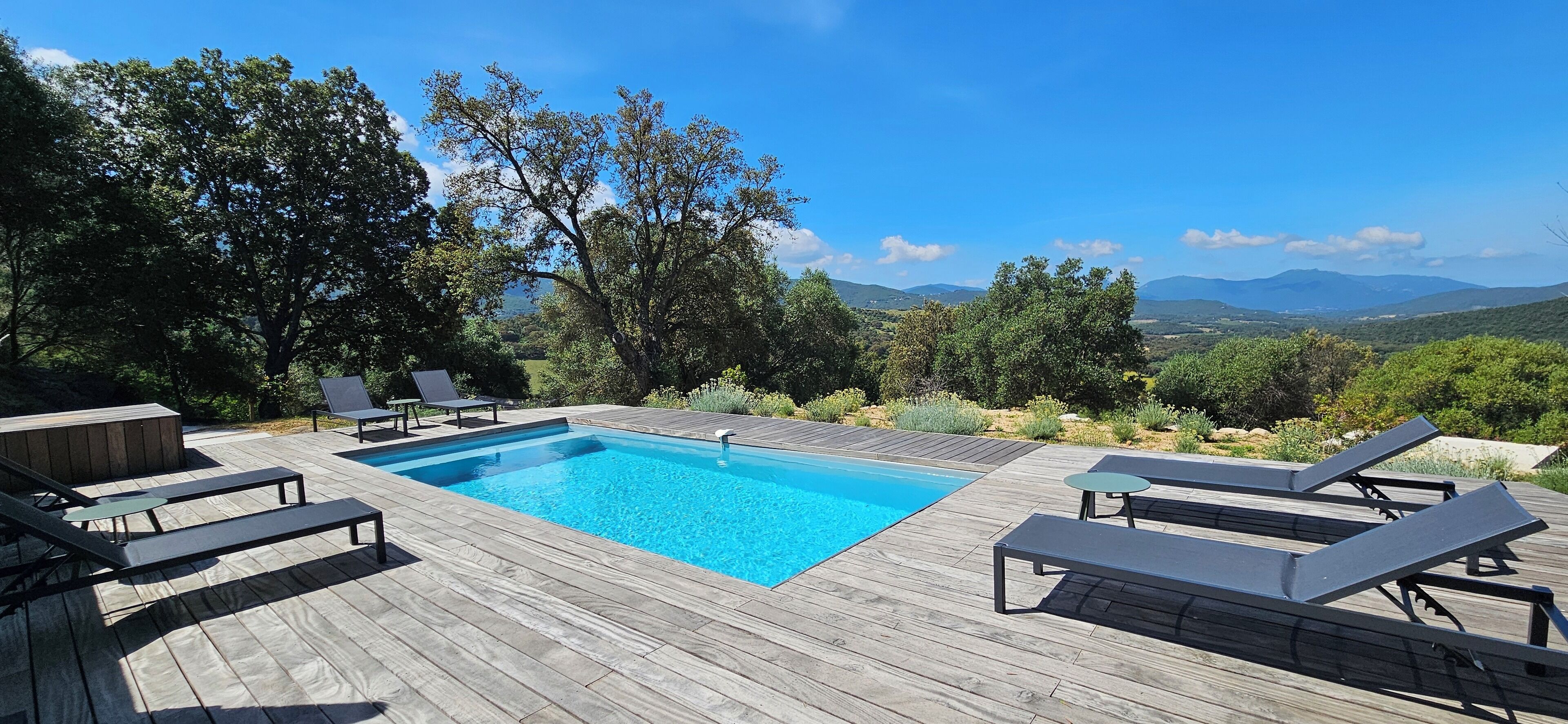 A wooden deck with a swimming pool, lounge chairs, and a hot tub.