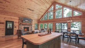 A spacious kitchen with a large island, wooden ceiling, and large windows offering views of the outdoors. - Make Memories In This Top Notch Lakefront Cabin (Stone Lake)