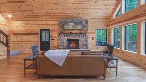 A log cabin interior with a stone fireplace, leather sofa, and large windows. - Make Memories In This Top Notch Lakefront Cabin (Stone Lake)