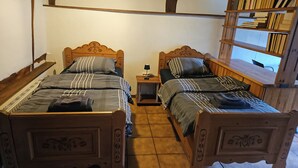 Una habitación con dos camas de madera, cada una con cabecero, una mesita de noche con lámpara y una estantería.