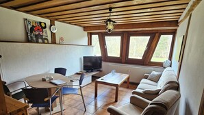 Interior acogedor de una cabaña con techo de madera, una zona de comedor con mesa y sillas, un sofá y una televisión.