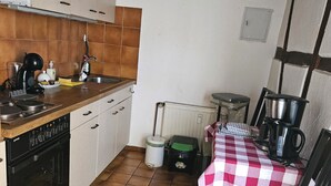 Una cocina compacta con estufa, lavamanos y un pequeño comedor con mantel a cuadros.