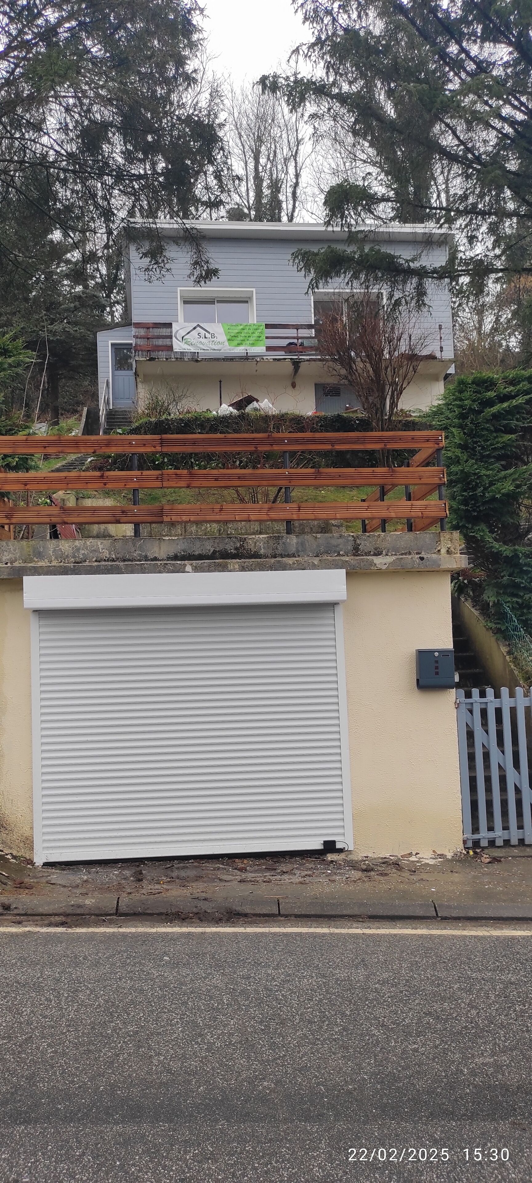 Een woongebouw met een garage, een houten hek en een naambord.