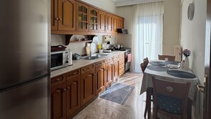 Cocina compacta con armarios de madera, refrigerador de acero inoxidable, microondas y zona de comedor con mesa y sillas.